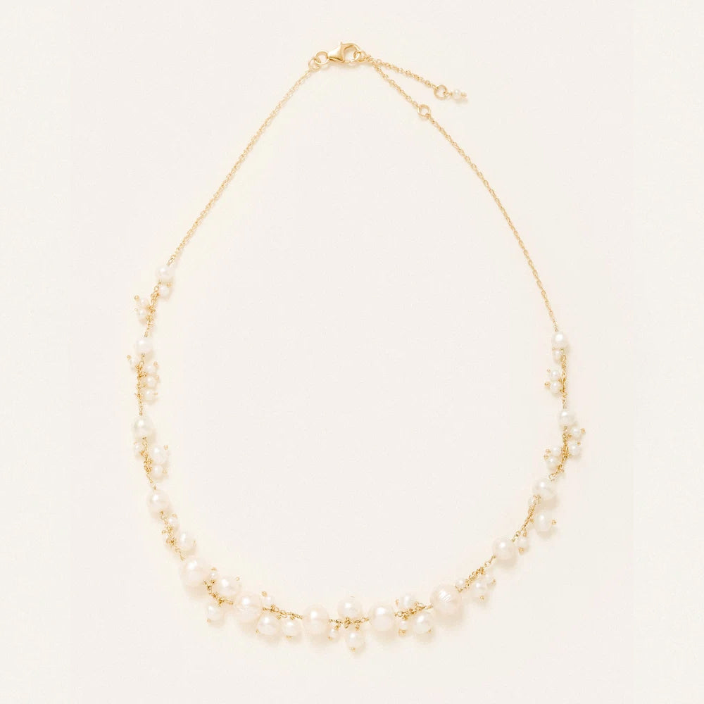 A delicate gold chain necklace adorned with pearls arranged in a curved, tiered design, displayed on a clean off white background.