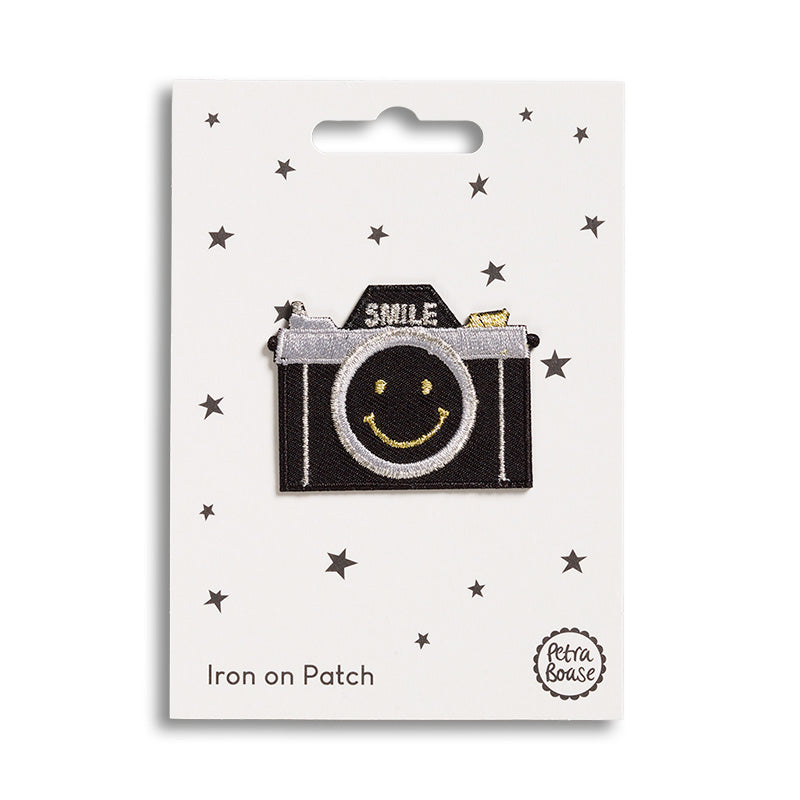 An iron patch featuring a classic black camera with the word 'smile' above and a smiley face on the lens.
