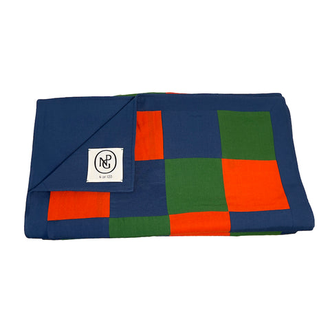 Neatly folded chequered table runner in orange and green with the top layer folded down exposing the NPG logo.