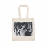 Natural beige tote bag with handles, featuring a black and white photograph of a woman in a dress and pearl necklace lying down. 