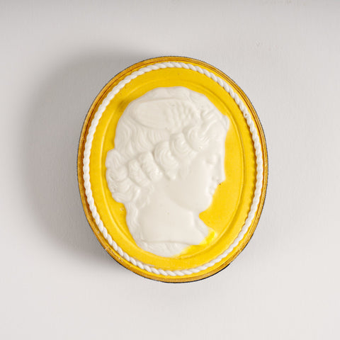 Oval paperweight in yellow and white featuring a profile portrait of a woman's head. 