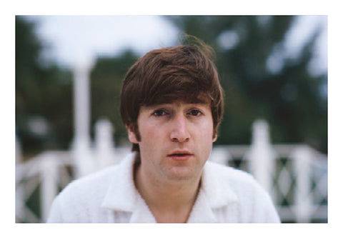 Colour photograph postcard of John Lennon in a white shirt with trees in the background, taken by Paul McCartney.