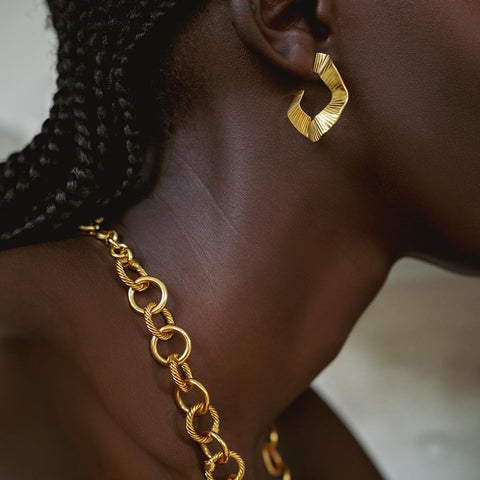Model wearing a gold metal loop with textured details and a gold chain.