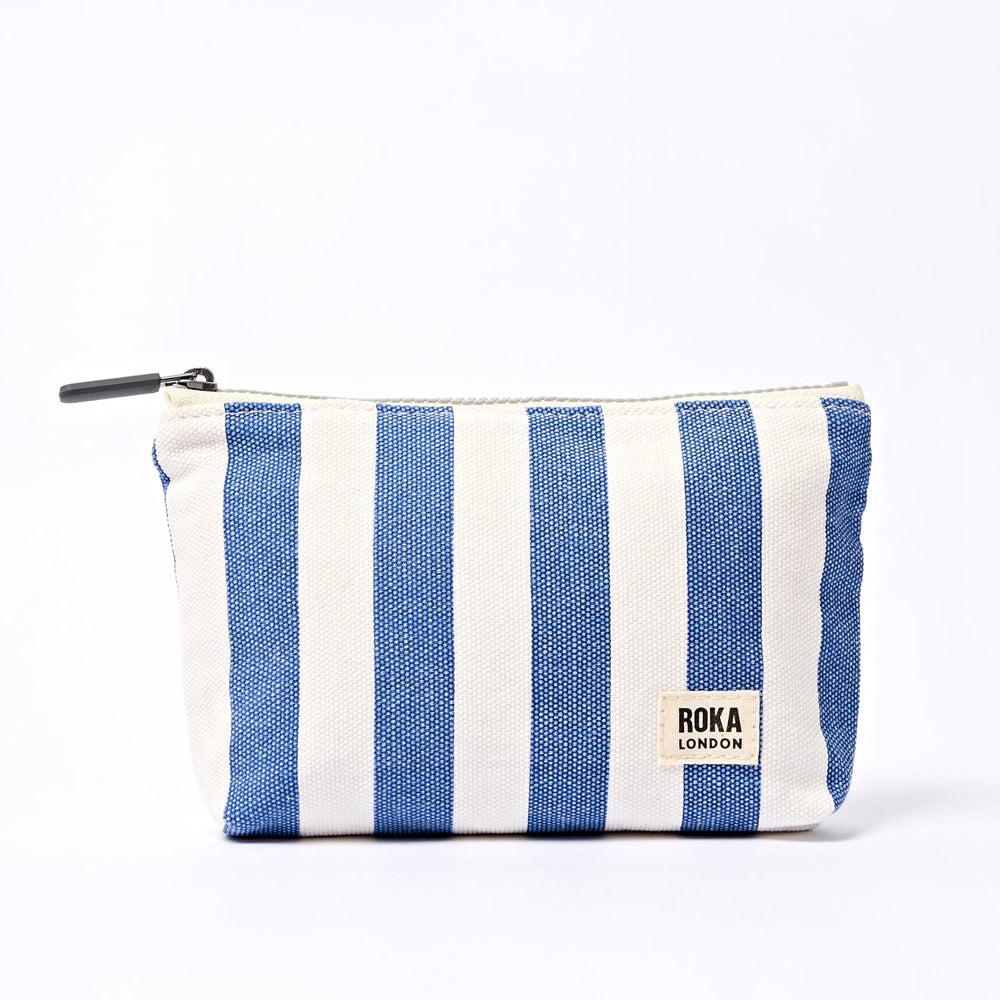 A rectangular zippered pouch with vertical blue and off white stripes, featuring a small white brand label that reads 'roka london' on the lower right side.
