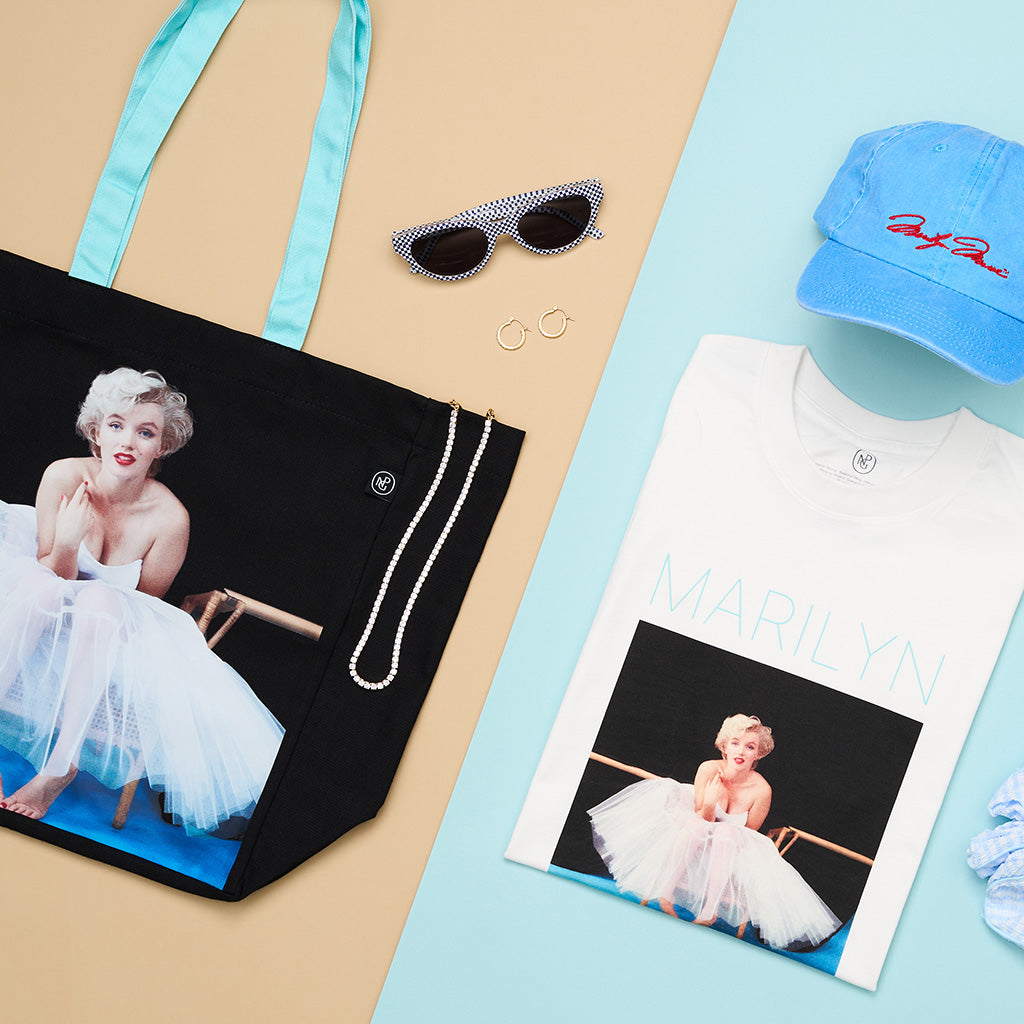 A selection of products including a tote bag and t shirt with an image of a woman sitting in a tutu, hat and glasses against a blue and beige background.