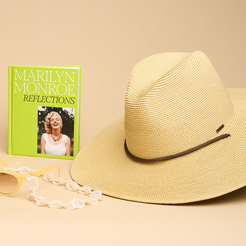 A straw hat and green book titled 'marilyn monroe reflections' against a beige background.