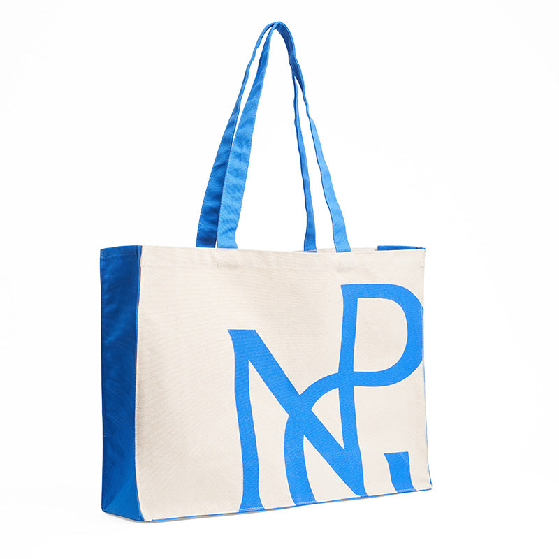 Side view of a wide cream tote bag with blue sides and handles and npg monogram design in blue.