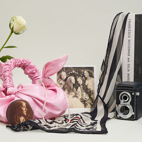 A pink bag is surrounded by accessories and a single rose. 