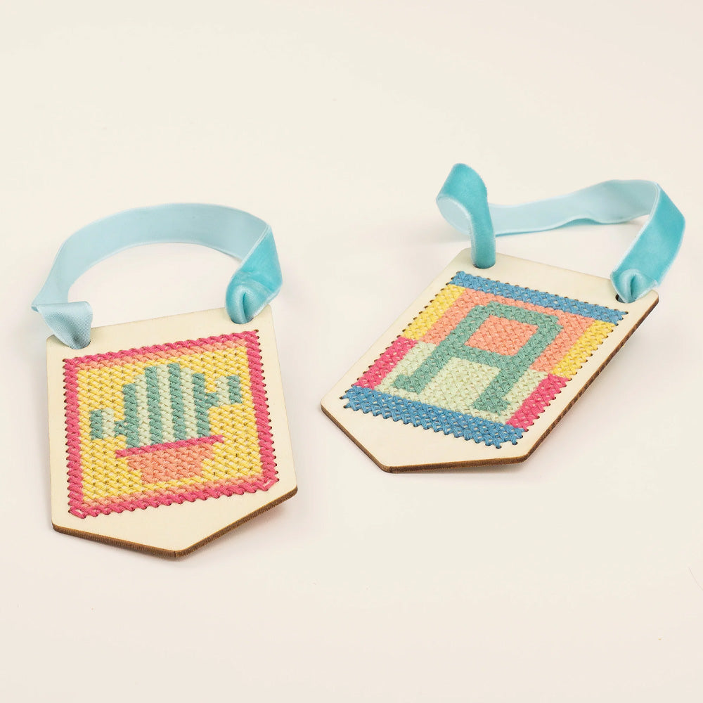 A pair of stitched banners, one with a cactus and one with the letter a against a beige background.