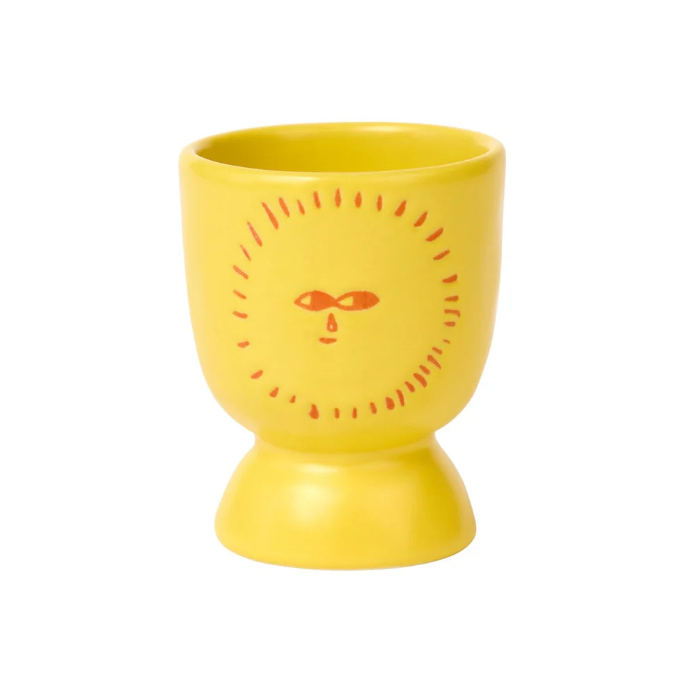 Yellow ceramic egg cup with a sun face design on a white background