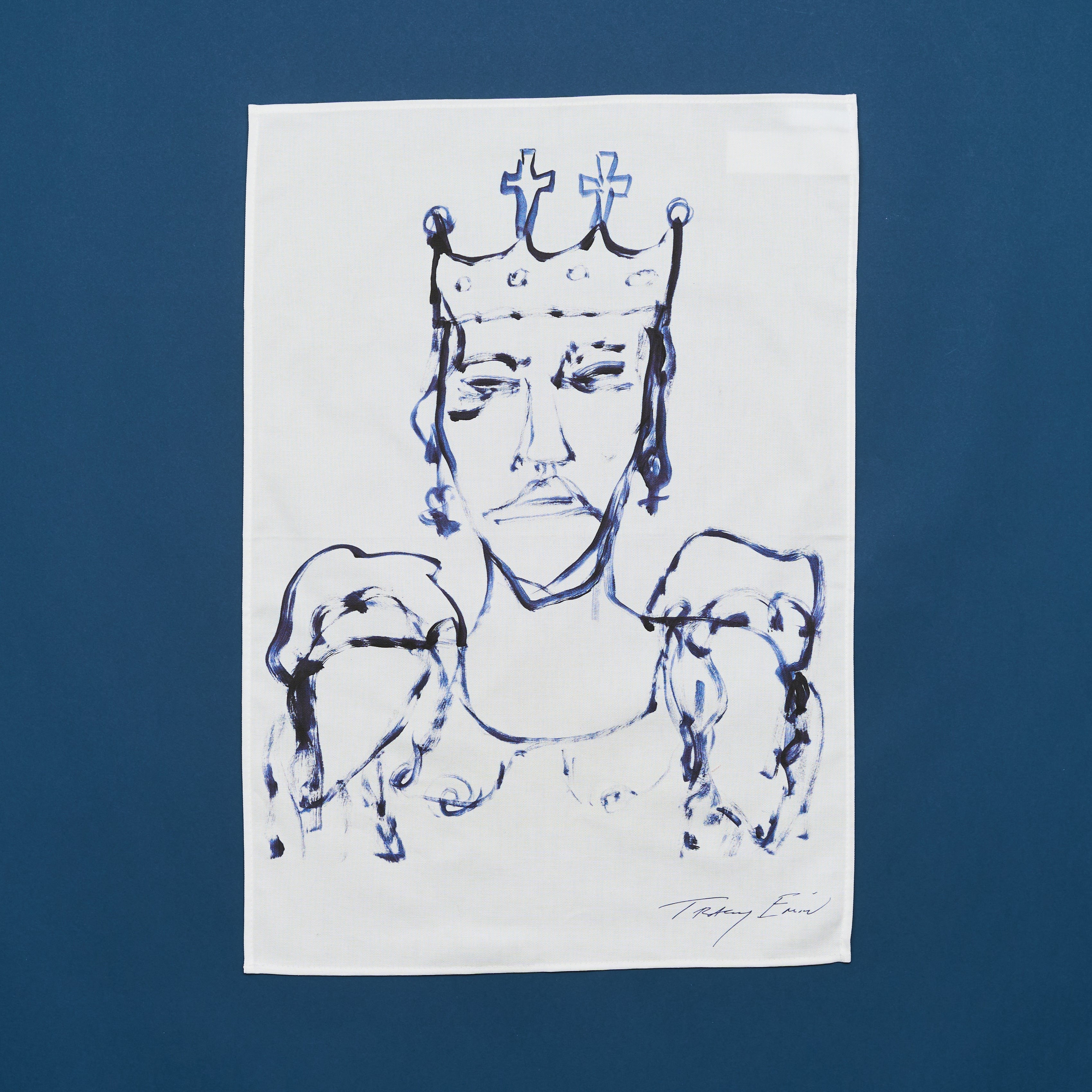 A white cotton tea towel with a blue transfer print featuring a portrait of a woman wearing a crown, with folds and the artist's signature at the bottom.
