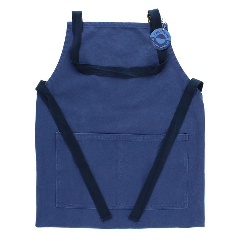 Blue apron with front pocket and dark contrasting neck strap and waist tie, with 'two tone utility apron' label.