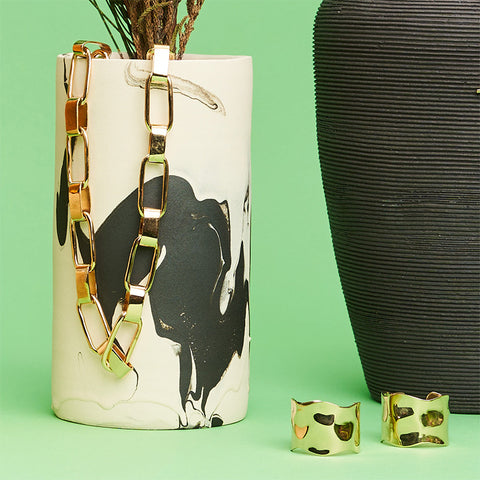 A pair of gold earrings and gold chain necklace hanging from a ceramic vase. 