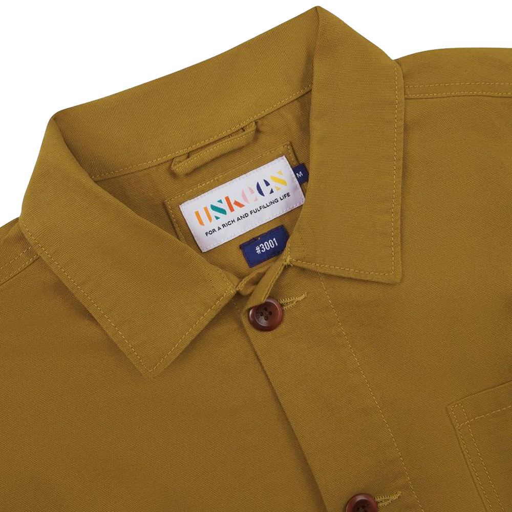 Close up of a mustard yellow shirt with a brand label on a white background