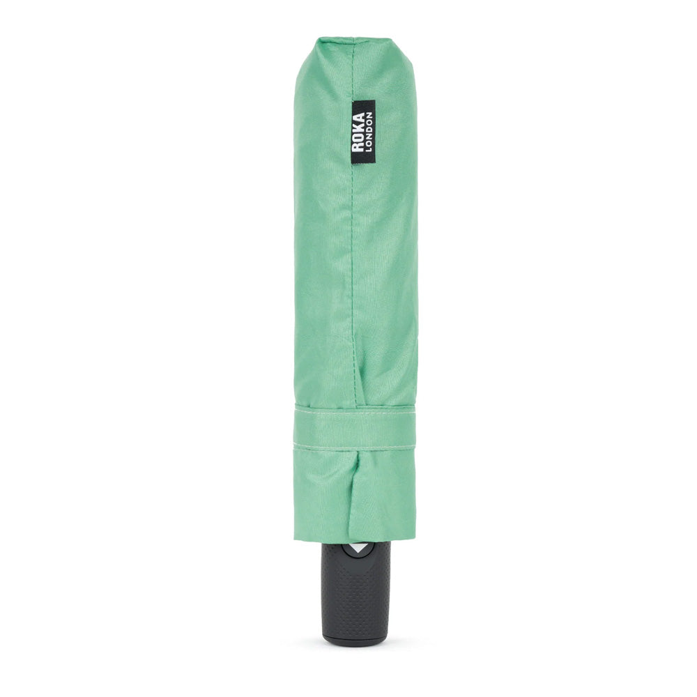 A mint green folded umbrella cover with a black roka brand label, shown vertically on a plain white background.