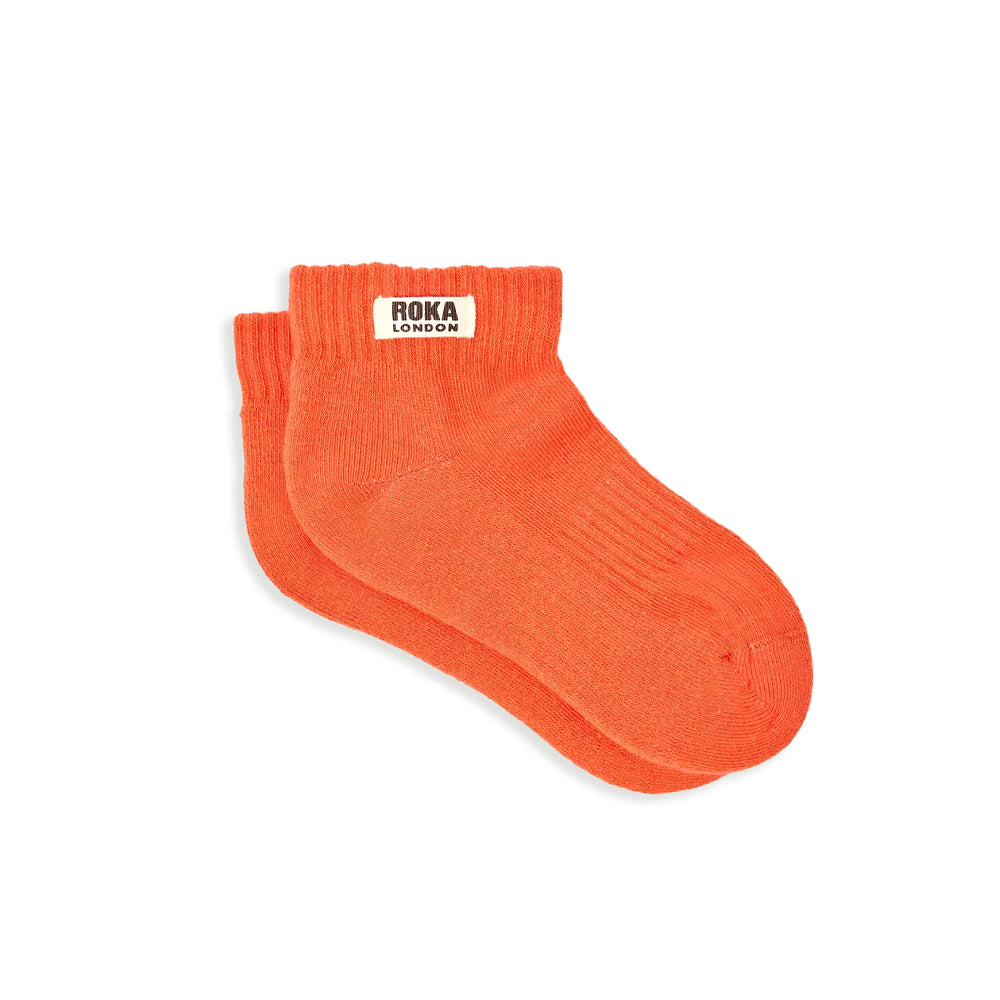 A pair of ribbed orange socks with a white label and the words roka london in black against a white background