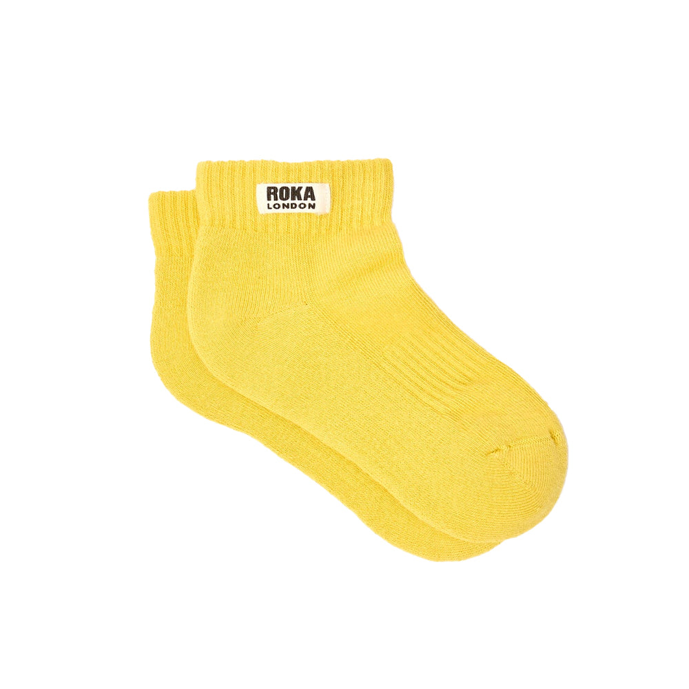 A pair of ribbed yellow socks with white label and the words roka london against a white background