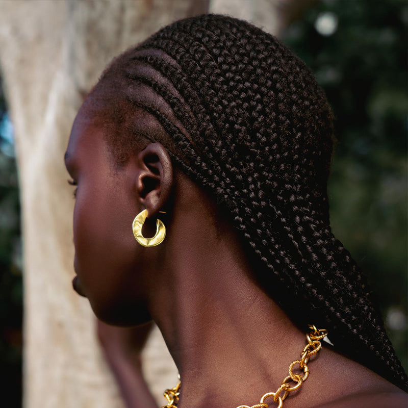Model wearing hook shaped gold earrings and a going chain necklace.