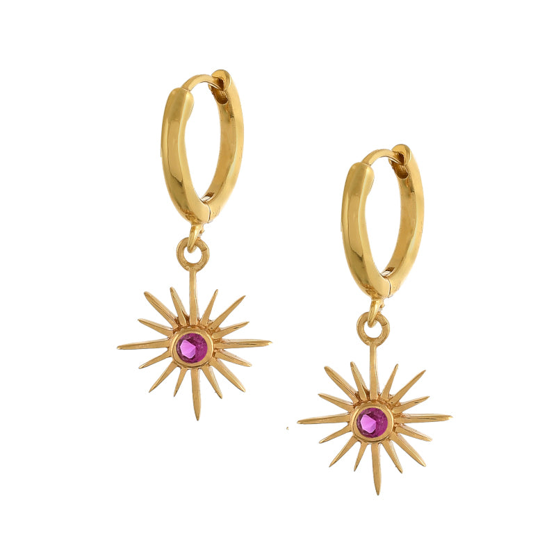 Felicity star ruby red earrings hanging from a gold huggie band.