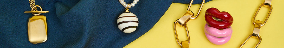 A selection of jewellery including lip shaped rings and a gold chunky chain necklace against blue fabric and a yellow background.