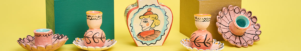 Image: a selection of hand painted ceramic candlesticks with floral motifs and a vase with an illustrated portrait.