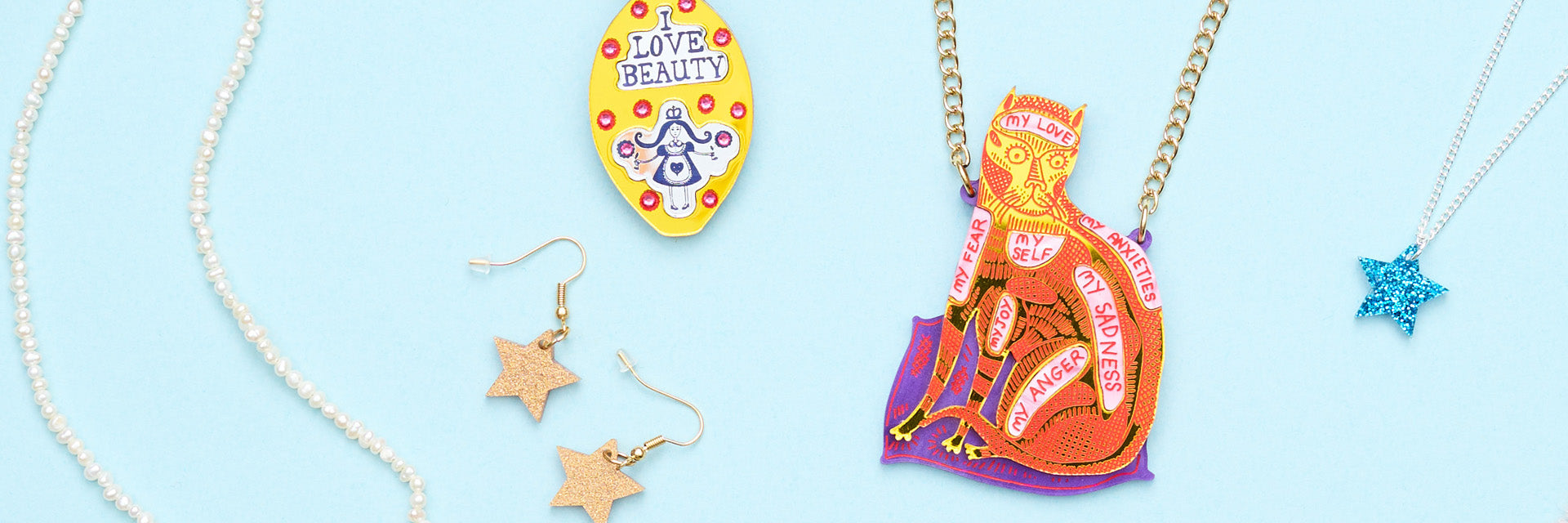 A selection of jewellery against a blue background including a cat pendant and star earrings.