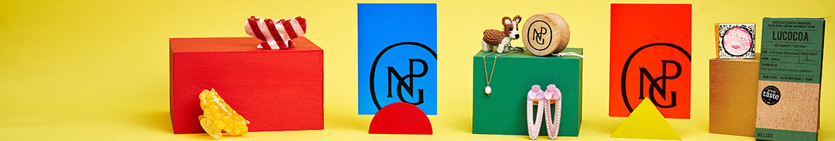 A selection of block colour gifts including npg notebooks and hairclips arranged on colourful blocks against a yellow background.