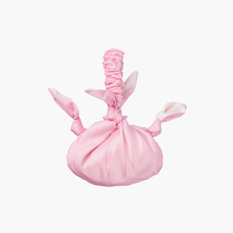 A round pink satin bag with knot details and a scrunchie style handle. 