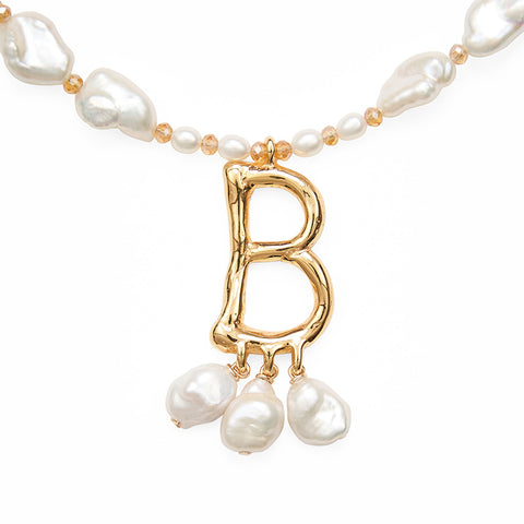 A close up view of a gold letter 'B' pendant and three hanging pearls below hanging from a pearl strand necklace.