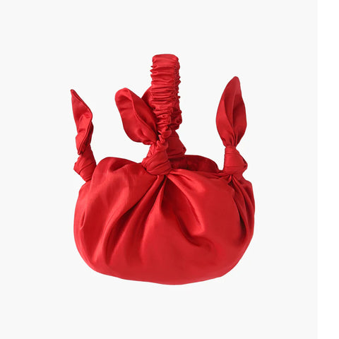 A round fabric bag with knot detailing and scrunchie style handle in bright red.