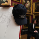 Black cap with 'WANTED' text on an easel in an art gallery setting