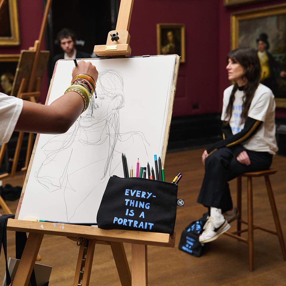 'everything is a portrait' pouch with pencils resting against an easel by a model posing in a gallery setting.