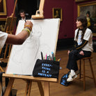 'Everything is a Portrait' pouch with pencils resting against an easel by a model posing in a gallery setting.