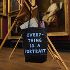 Black tote bag with 'Everything is a Portrait' text in a museum setting