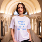 Person wearing a white t-shirt with blue 'Everything is a Portrait' text in an architectural setting
