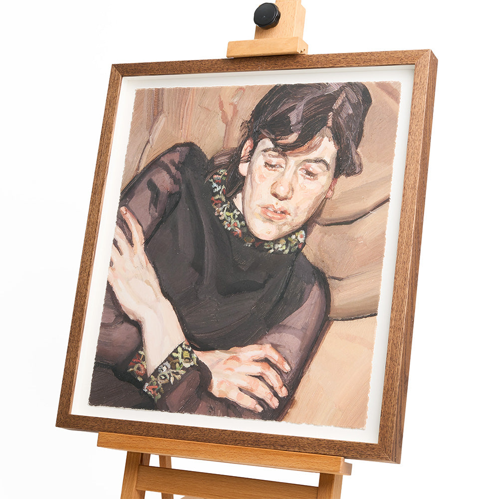 A framed print of a women in a black dress with her arms crossed, the framed rests upon a wooden easel.