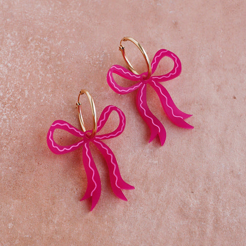 A pair of pink acrylic bow shaped earrings on gold hoops.  