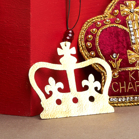 Crown shaped hammered brass decoration hanging from black thread with three red beads.