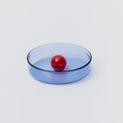 Round blue glass dish with central red bubble.