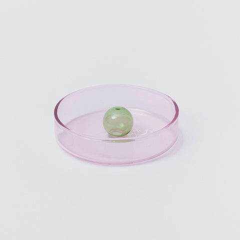 Round pink glass dish with central green bubble.