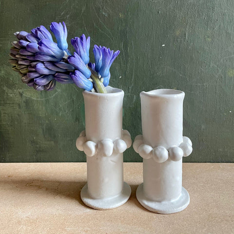 Two ceramic vases with ball detailing holding a blue flower stem.