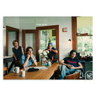 Poster of four people sitting around a table in a room with large windows, featuring the title Catherine Opie: To Be Seen.