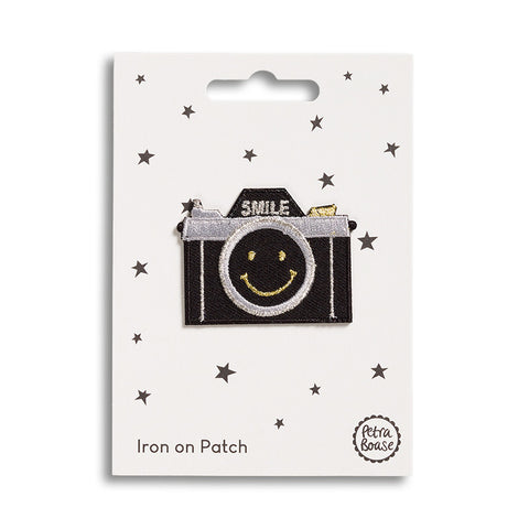 An iron patch featuring a classic black camera with the word 'Smile' above and a smiley face on the lens. 
