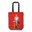 Red tote bag with an image of a person sitting on a stool on a white background