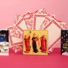 Christmas notecards displayed in a fan shape alongside other standing Christmas cards, against a pink background.
