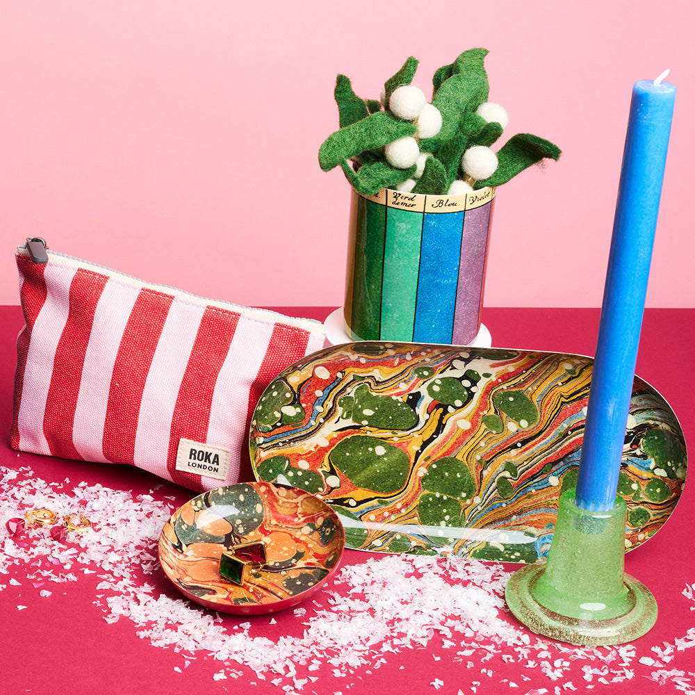 Styled setup of a striped canvas pouch, candles and marbled trays against a background of two contrasting pinks colours.