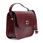 Maroon handbag with metal clasp and strap on a white background