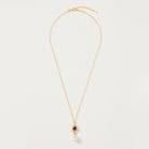 A delicate gold chain necklace featuring a small diamond-shaped pendant with a dark red gemstone and a dangling white pearl, displayed on a clean off-white background.