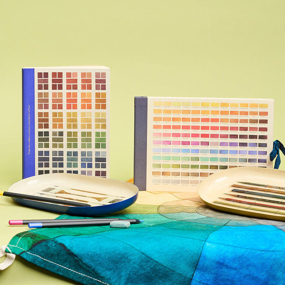 Colour swatches design sketchbook, journal and art supplies on a gradient colour tea towel against a green background.