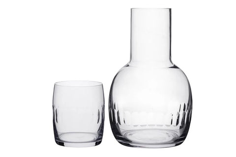 A glass carafe with a lens with a matching glass cup next to it. 